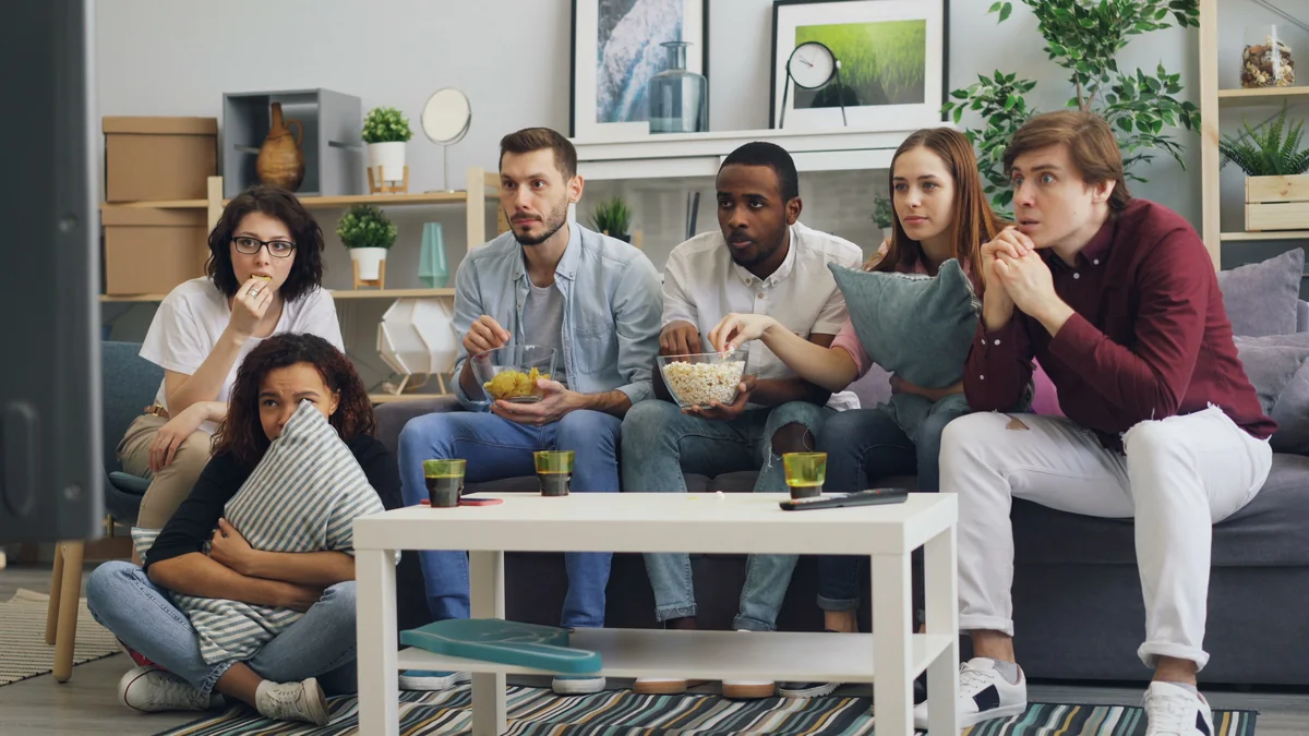 Six adults watching television together in a bright living room.